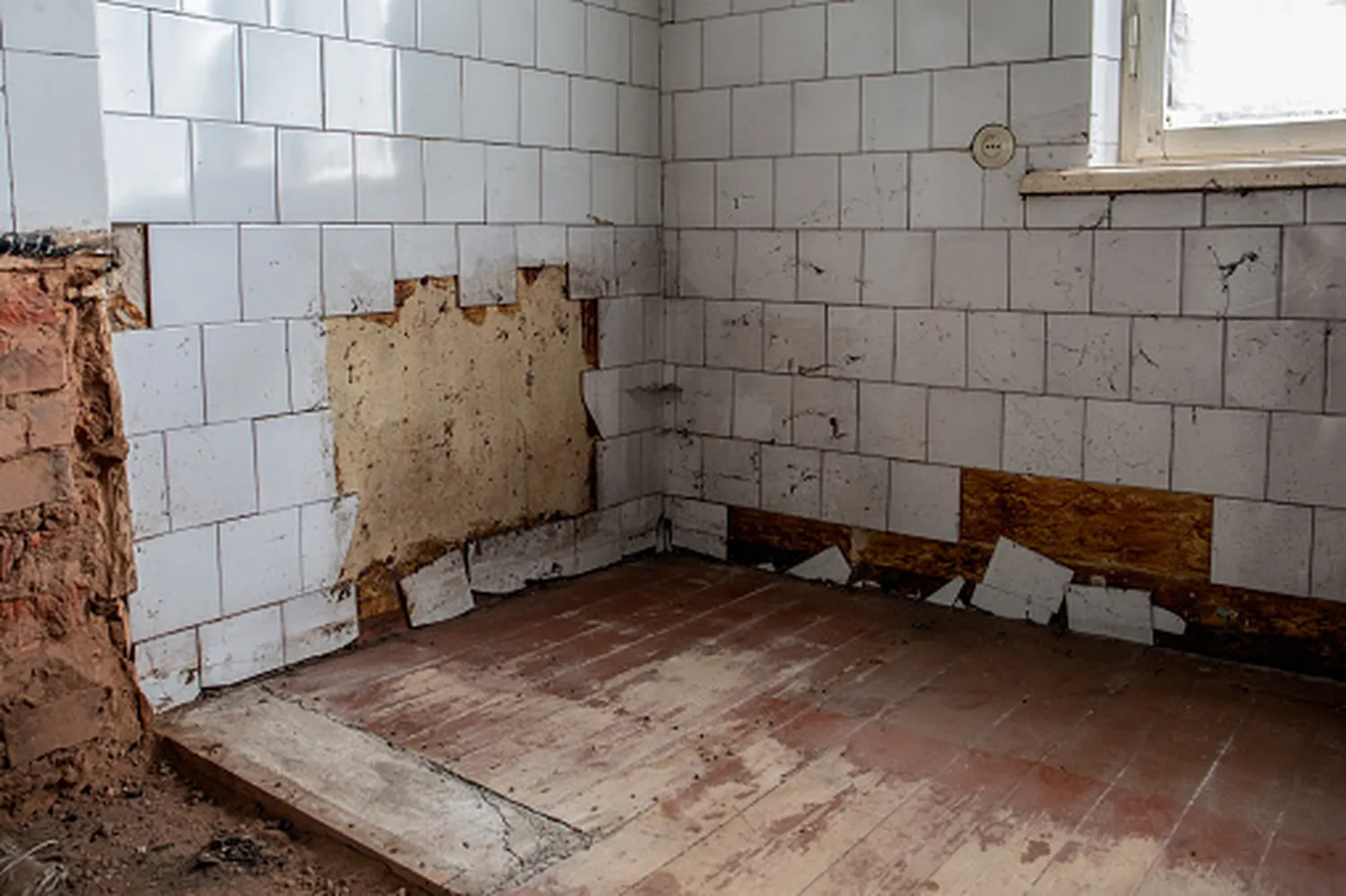 Kanzler Facility GmbH - Hausmeisterservice, Reinigung, sanierung & Wasserschadensanierung - Ein altes, schmutziges Zimmer in schlechtem Zustand mit bröckelnden Wänden, abblätternder Tapete und einem beschädigten Holzboden.